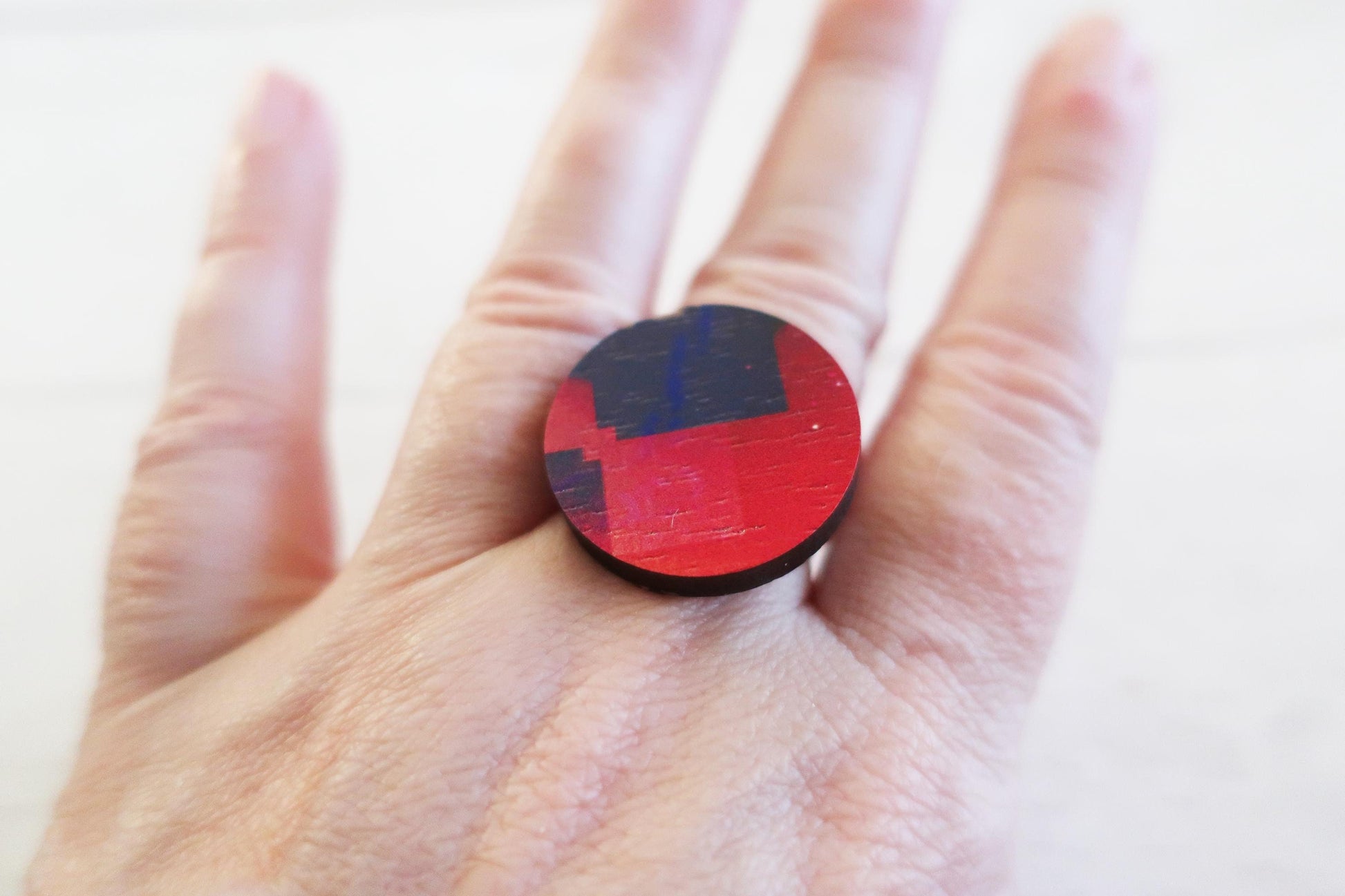 Hand wearing a red and blue ring with a geometric pattern on a white background