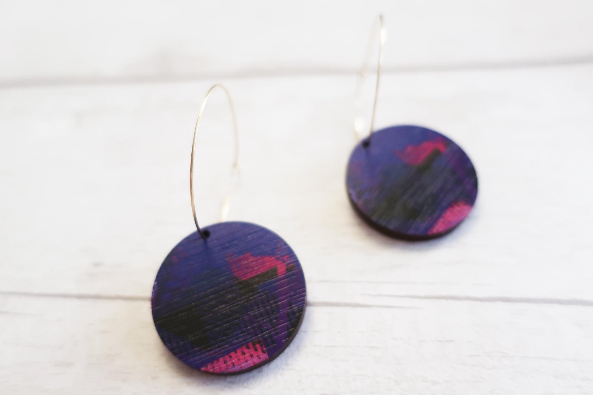 Pair of round earrings with purple and pink design on a white background