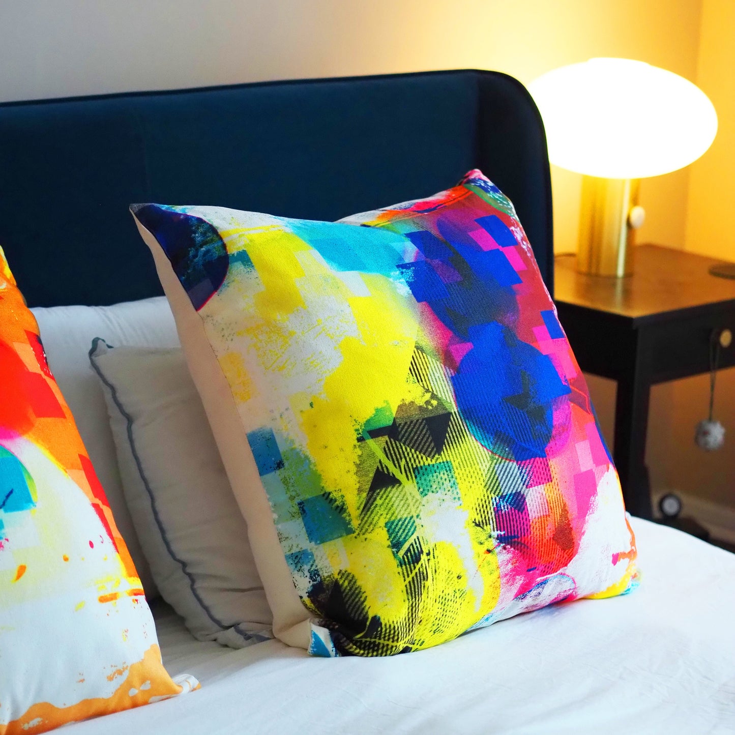 Colorful abstract-patterned pillows on a bed with a lamp in the background.