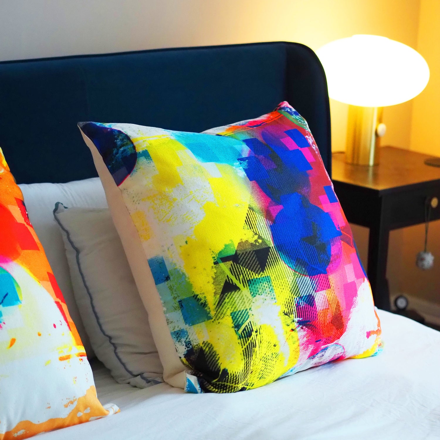 Colorful abstract-patterned pillows on a bed with a lamp in the background.