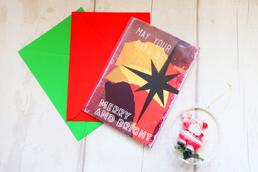 Greeting card with 'May your days be merry and bright' text, surrounded by colorful envelopes on a wooden surface.