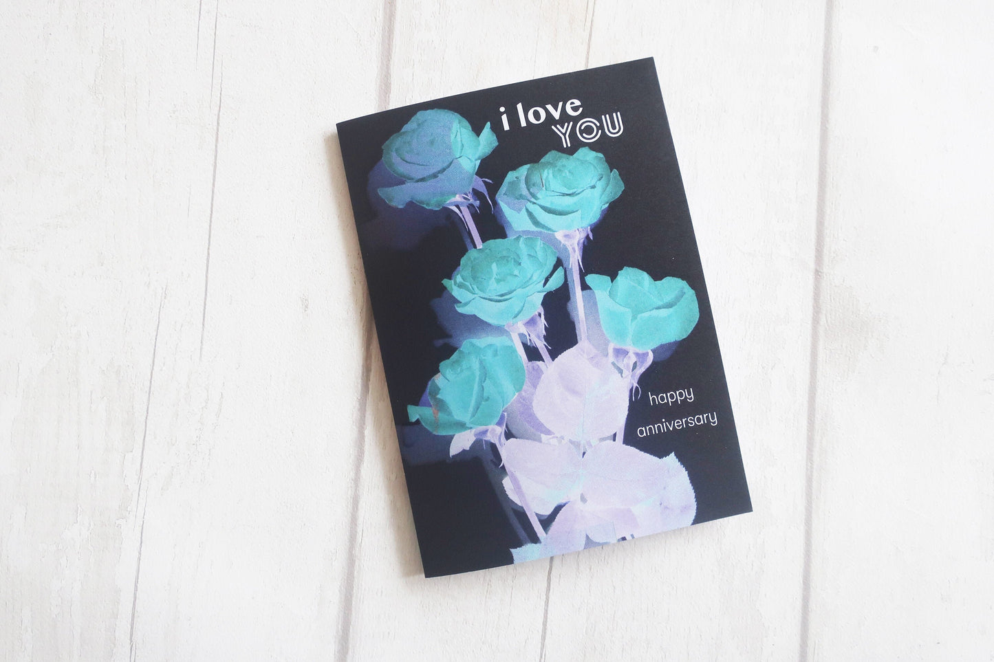 Greeting card with blue roses and 'I love you' text on a white wooden surface