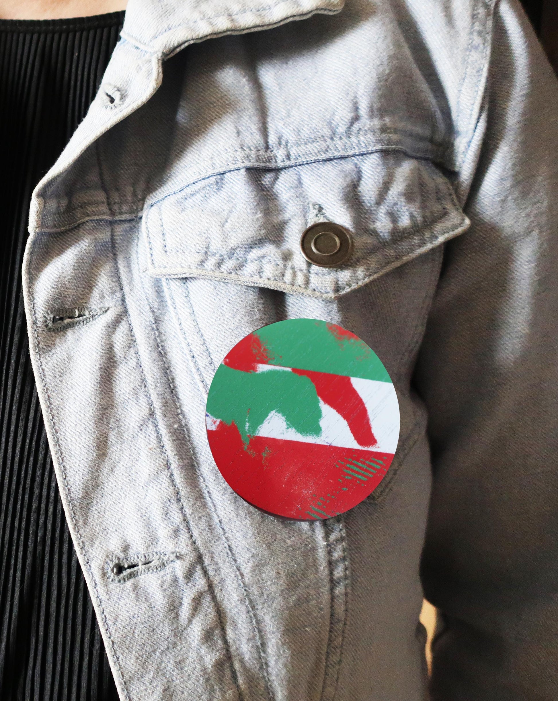 Light gray denim jacket with a round brooch featuring a green and red design on a dark background