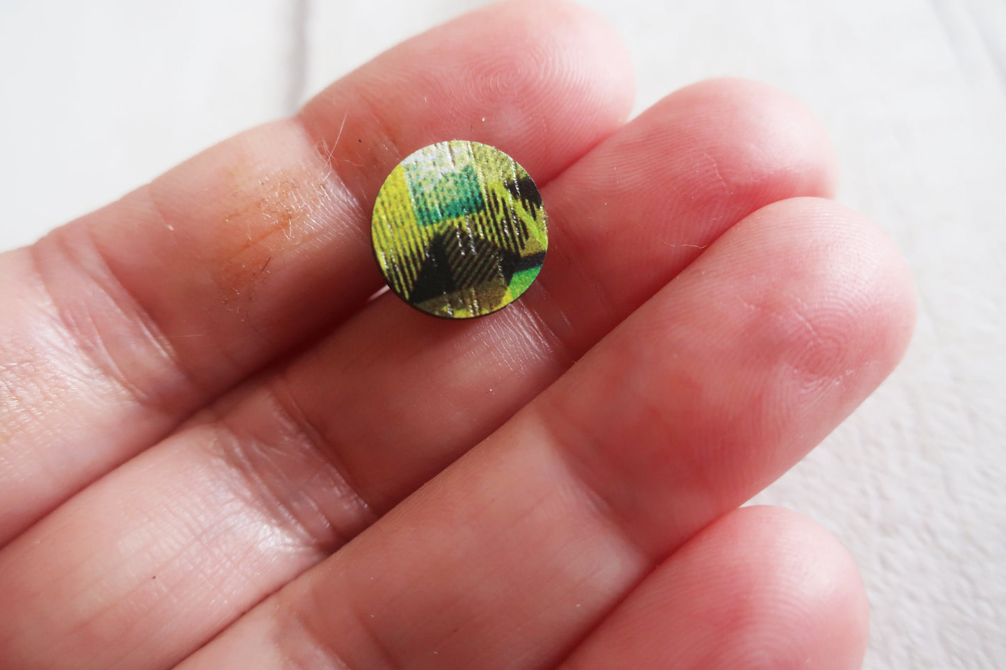 Round, multicolored earring held between fingers against a white background