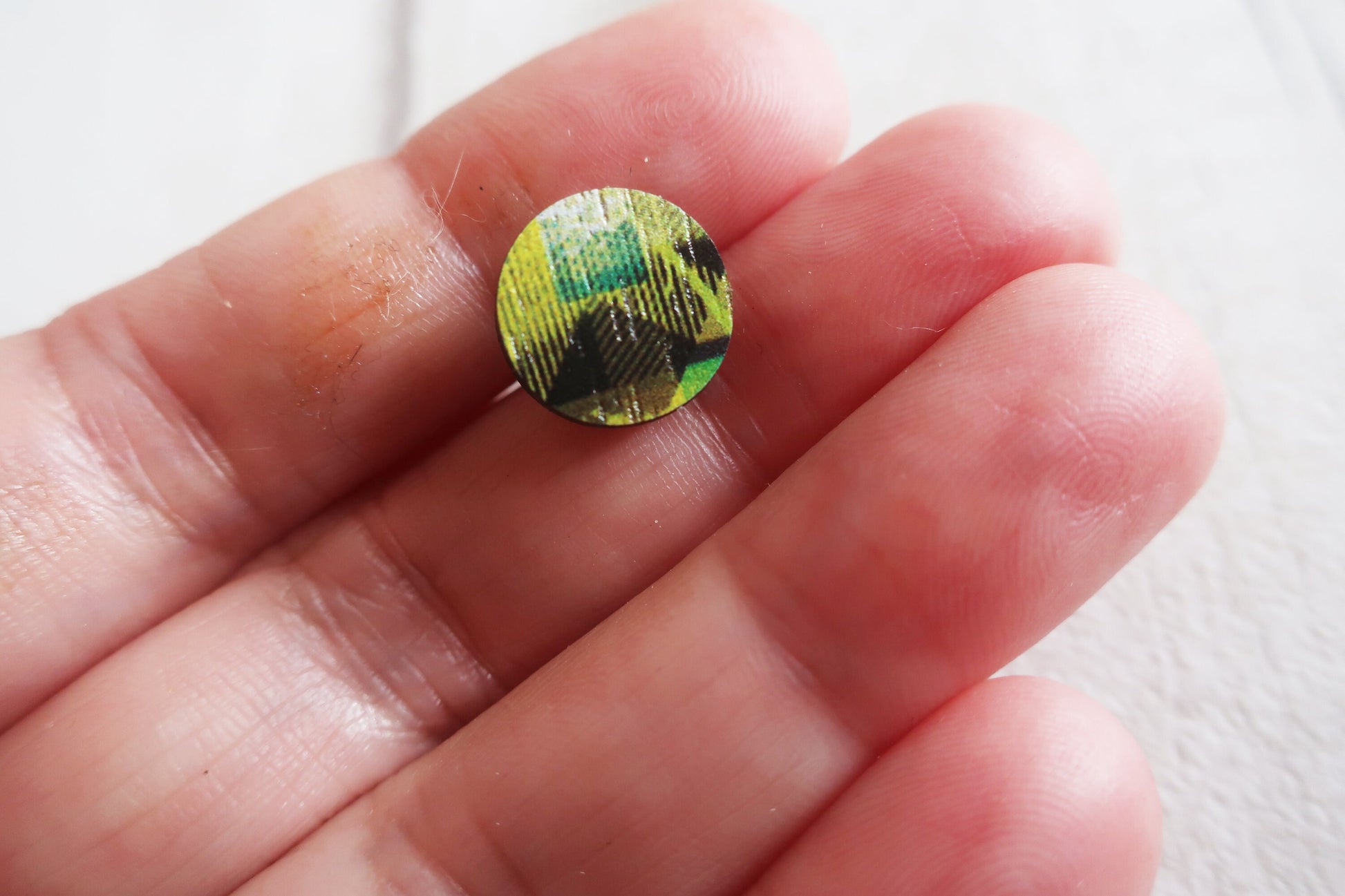 Round, multicolored earring held between fingers against a white background