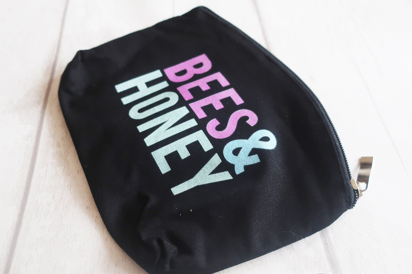 Black pouch with 'BEES & HONEY' text in pastel colors on a white background