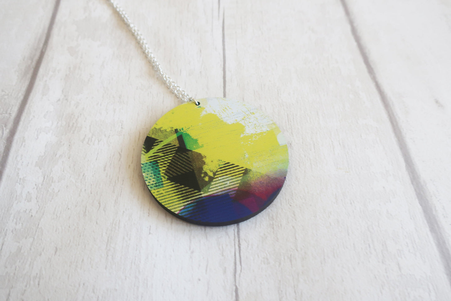 Colorful round pendant on a chain against a light wooden background