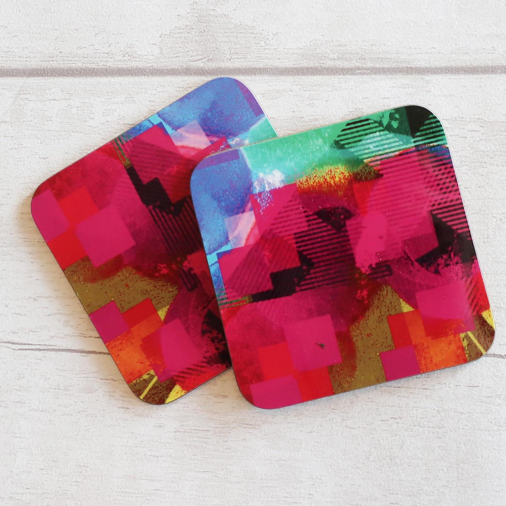 Two colorful square coasters on a light wooden surface