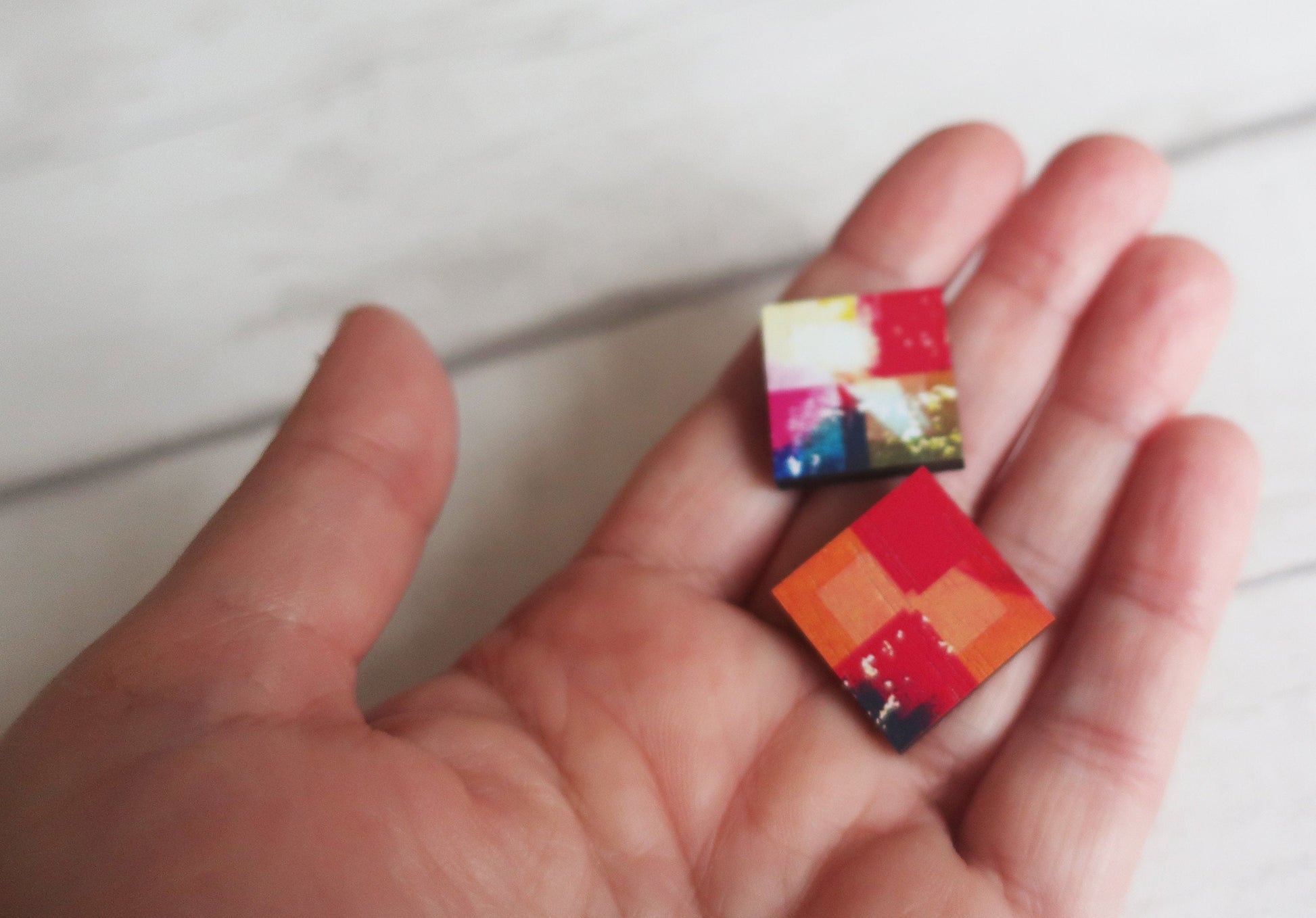 Colorful square earrings held in a hand against a white background