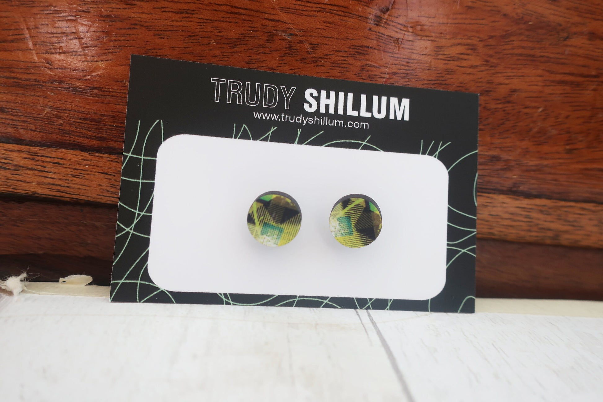 Pair of earrings on a Trudy Shillum branded card against a wooden background