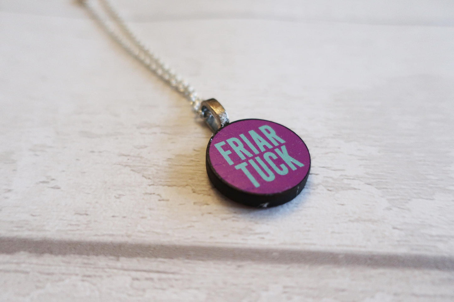 Necklace with a pendant displaying 'FRIAR TUCK' text on a light wooden surface