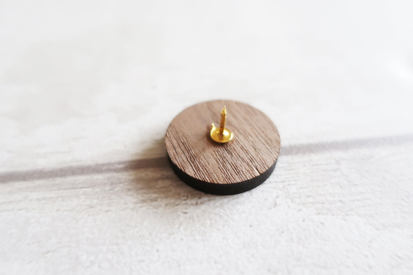 Wooden round pin badge with a gold spike on a white surface