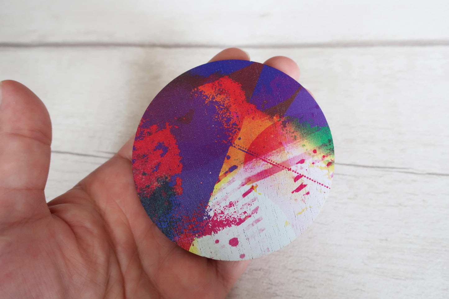 Colorful circular brooch held by a hand on a light wooden surface