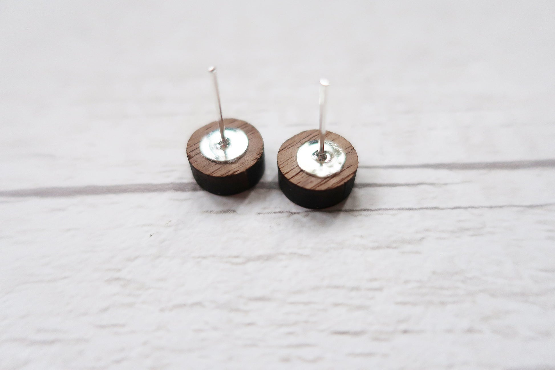 Pair of wooden earrings with silver tops on a light gray background