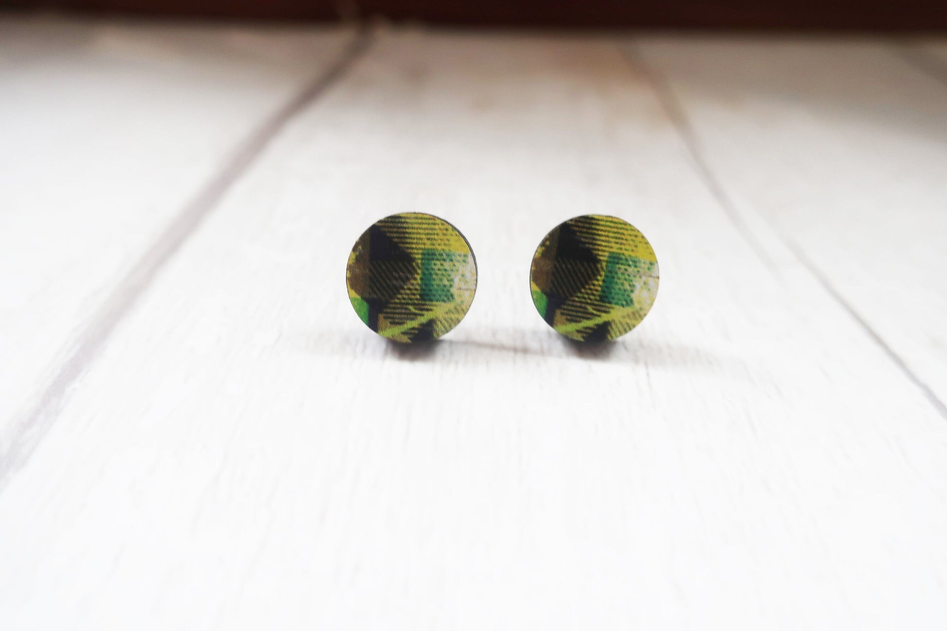 Round green and black patterned earrings on a white surface