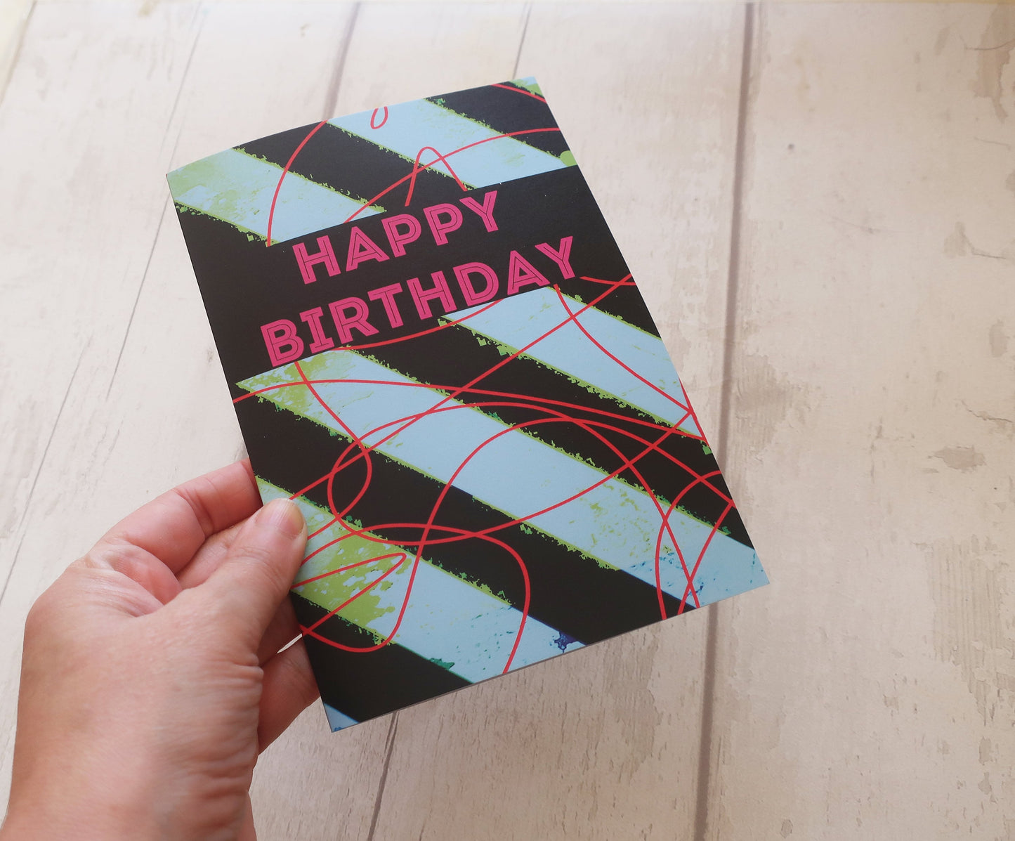 Hand holding a colorful birthday card with 'Happy Birthday' text on a wooden surface