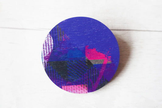 Round purple brooch with abstract pattern on a white surface