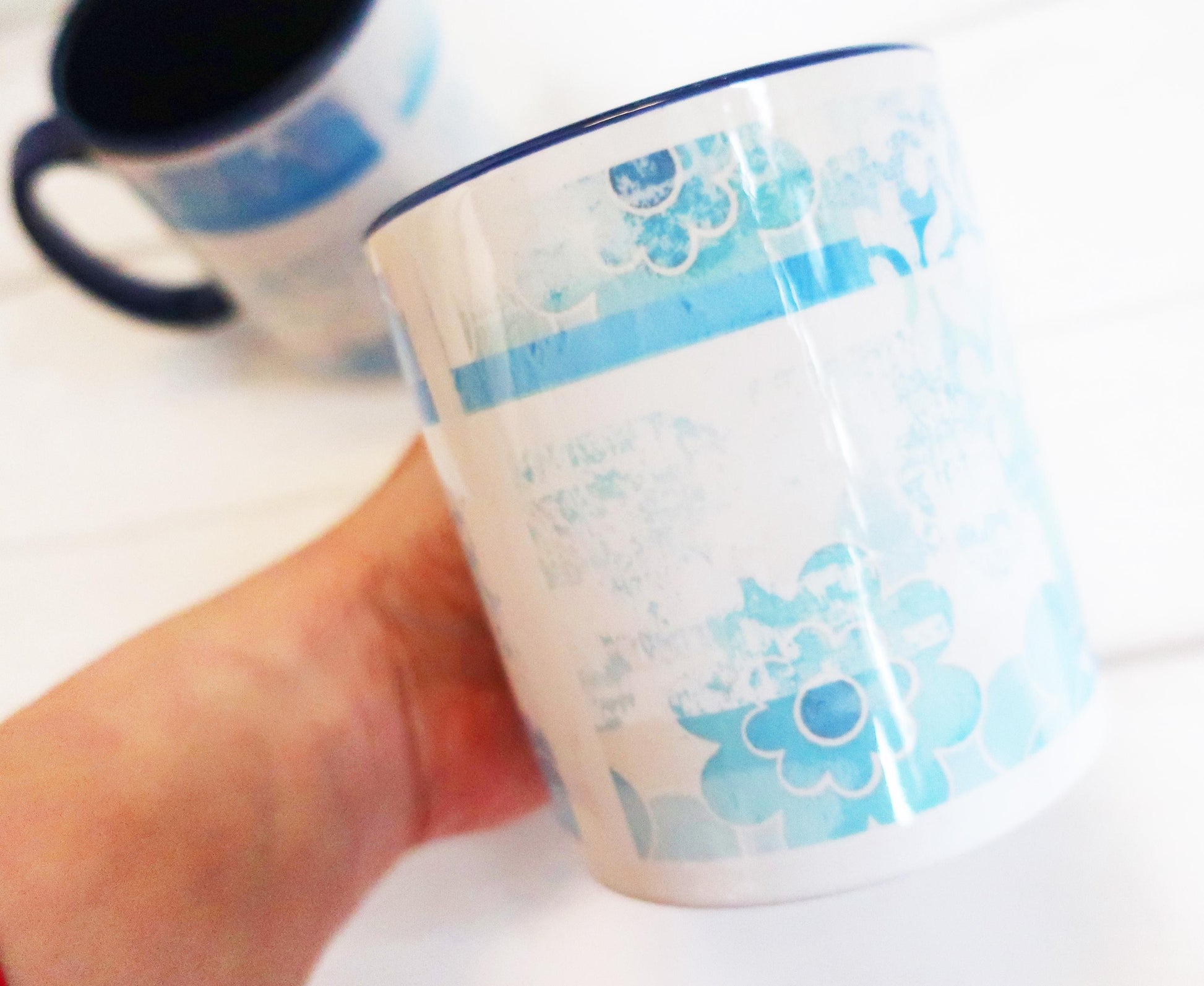 White mug with blue floral pattern held by a hand on a white background