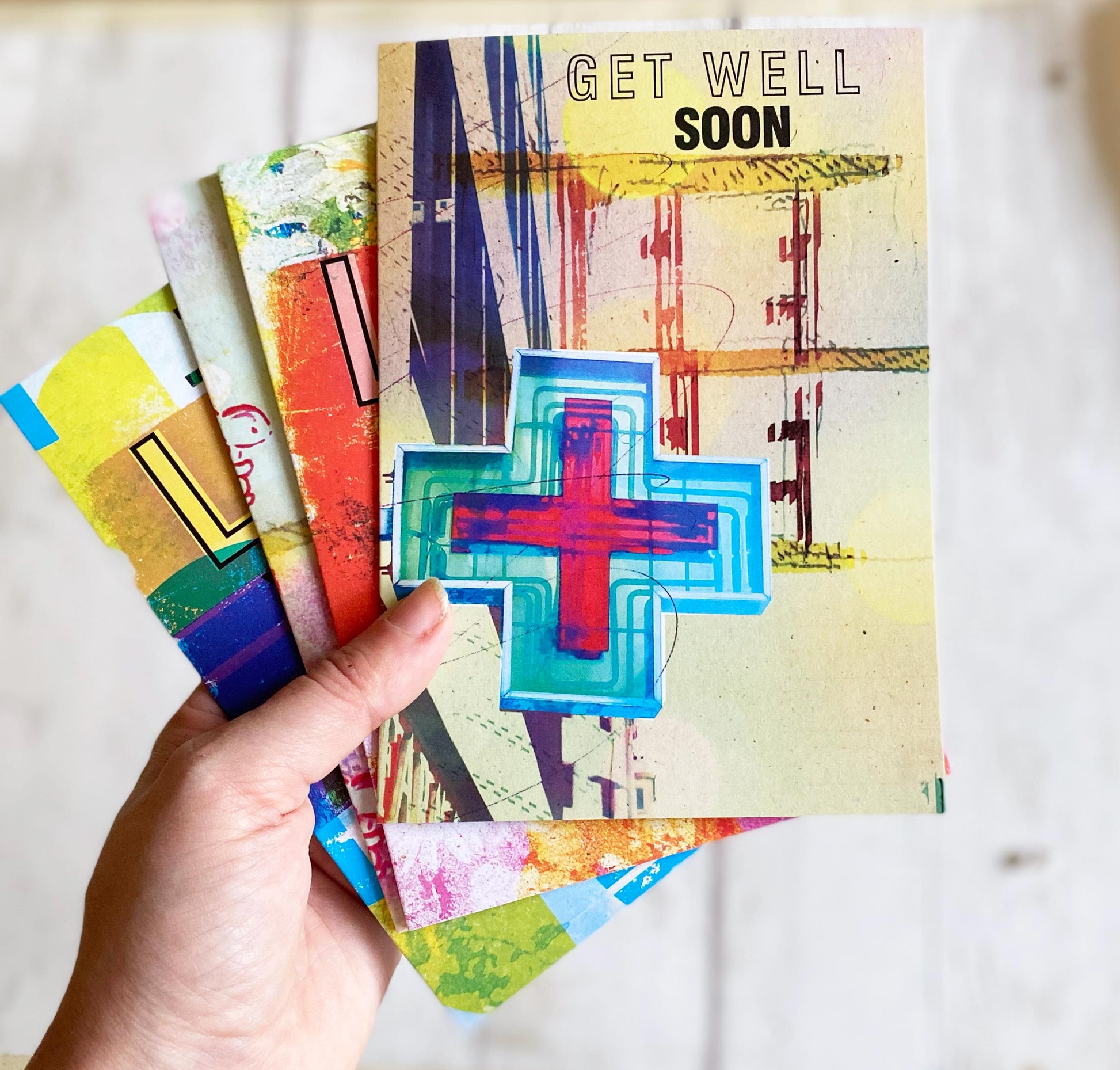 Colorful 'Get Well Soon' cards held by a hand on a light background