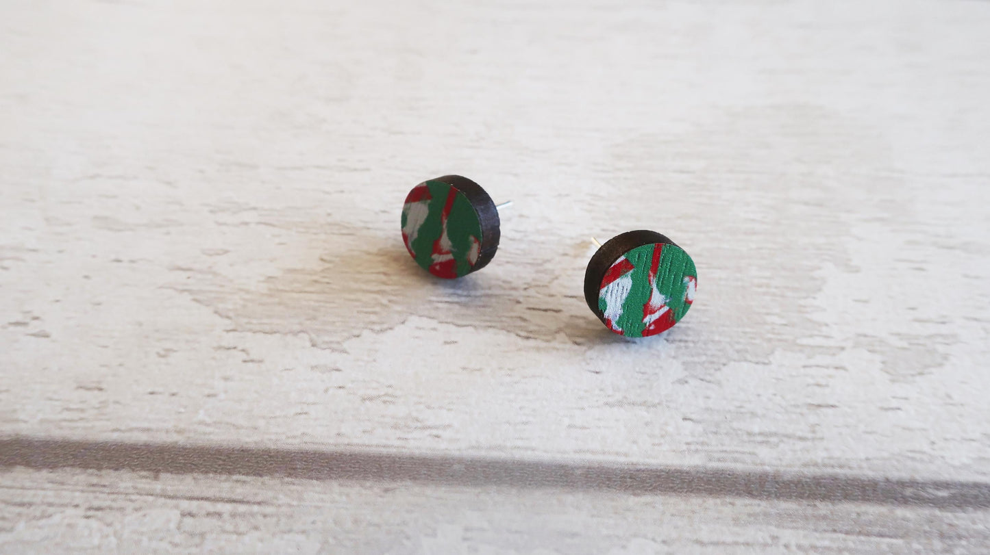 Pair of round earrings with a green and red pattern on a light wooden surface.