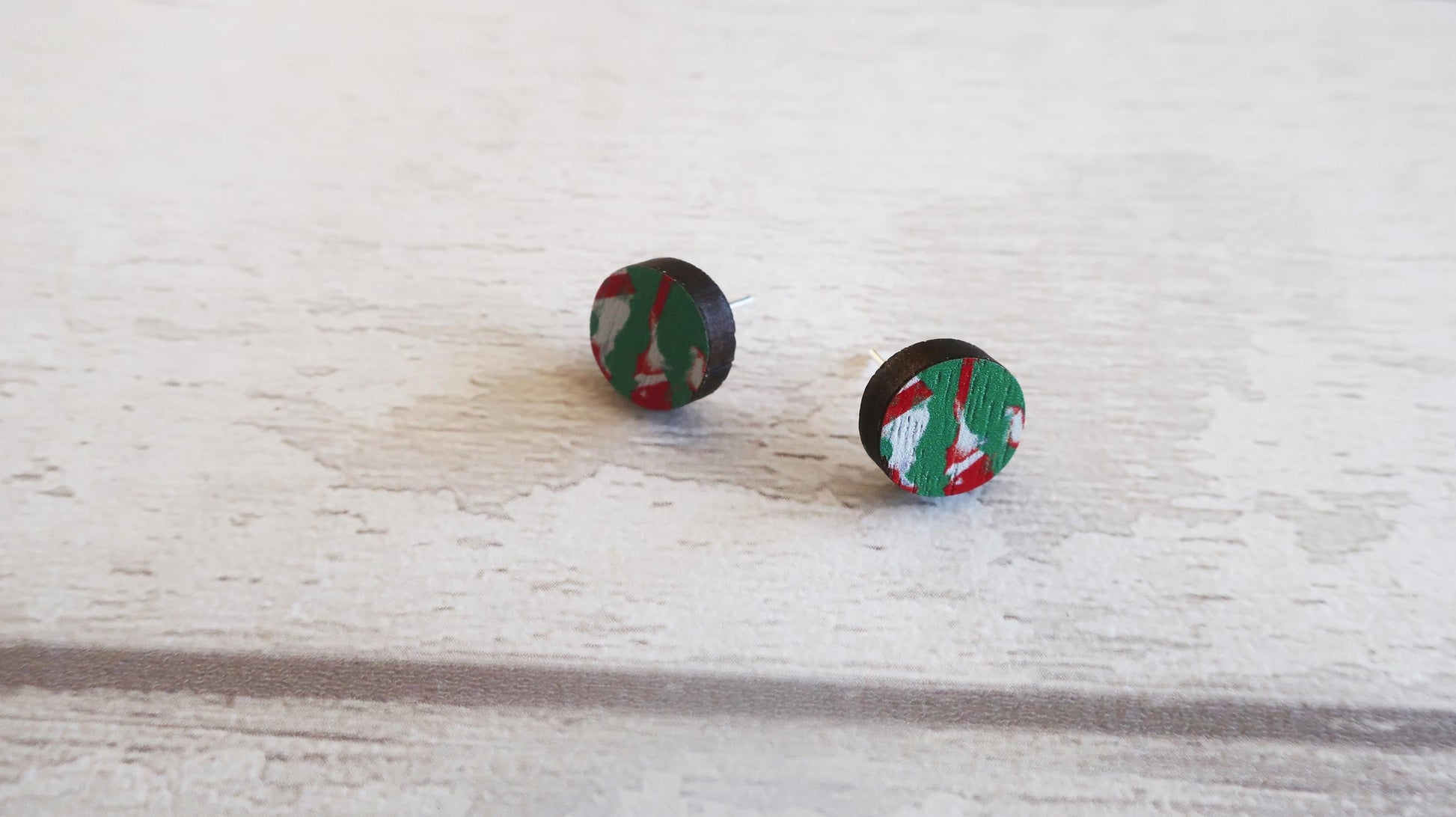 Pair of round earrings with a green and red pattern on a light wooden surface.