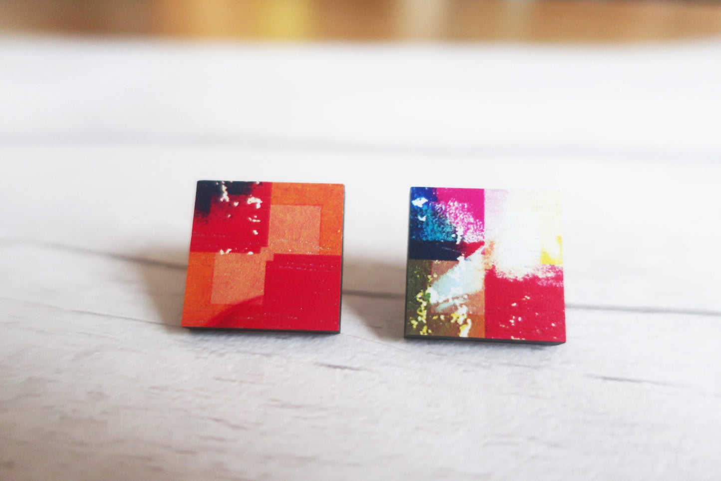Two colorful square earrings on a light wooden surface