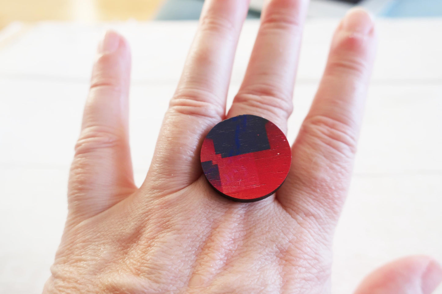 Hand wearing a red ring with blue design on a light background