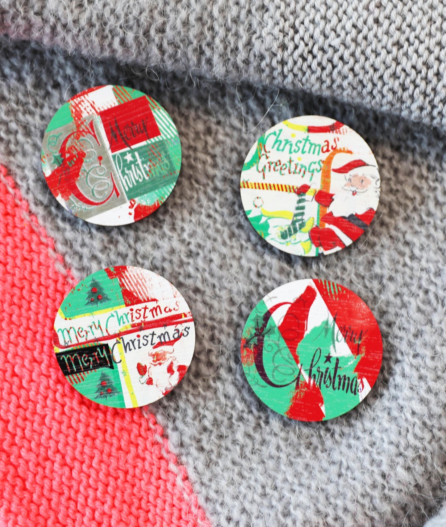 Four Christmas-themed button badges on a textured fabric background