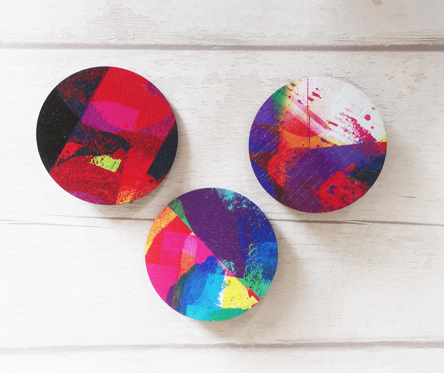 Three colorful circular brooches on a wooden surface