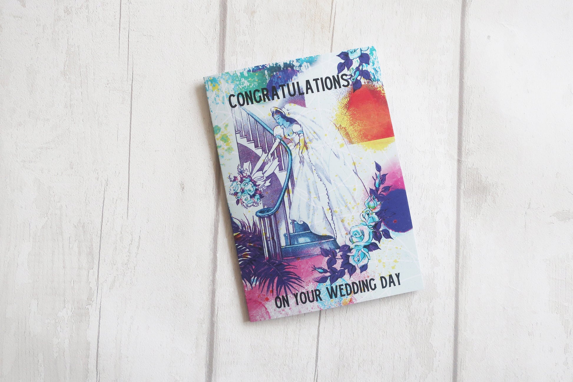 Wedding card with colorful design and 'Congratulations on your wedding day' text on a white wooden surface.