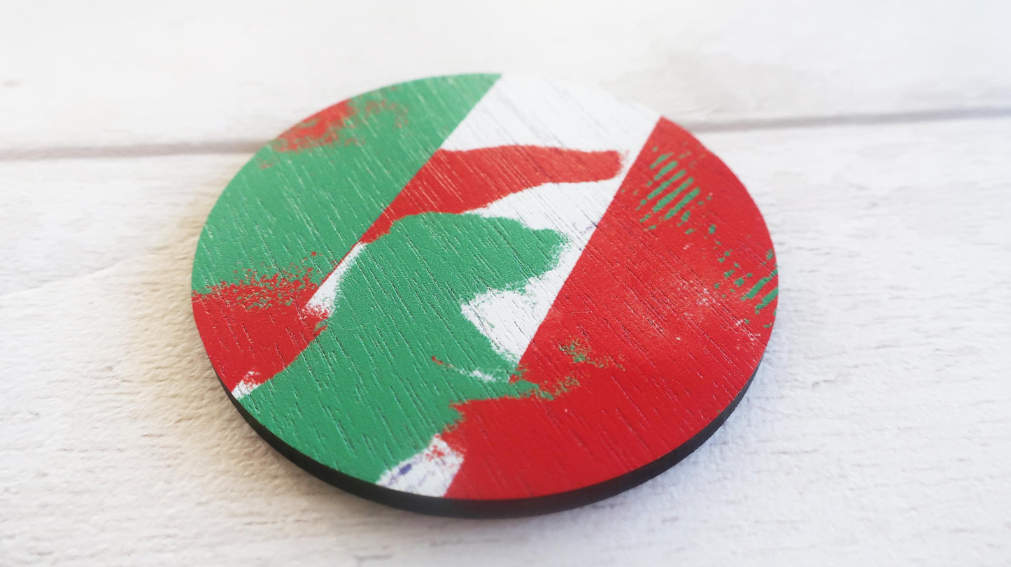 Round wooden brooch with red, green, and white design on a light wood surface