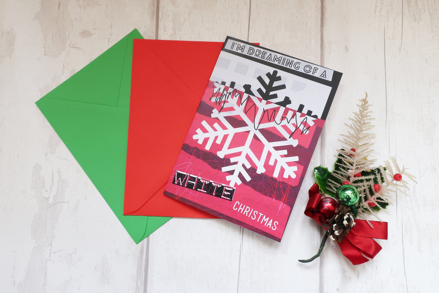 Christmas card with snowflake design and red and green envelopes on a light wooden surface.