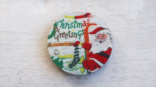 Round Christmas-themed badge with Santa Claus and text on a textured white background