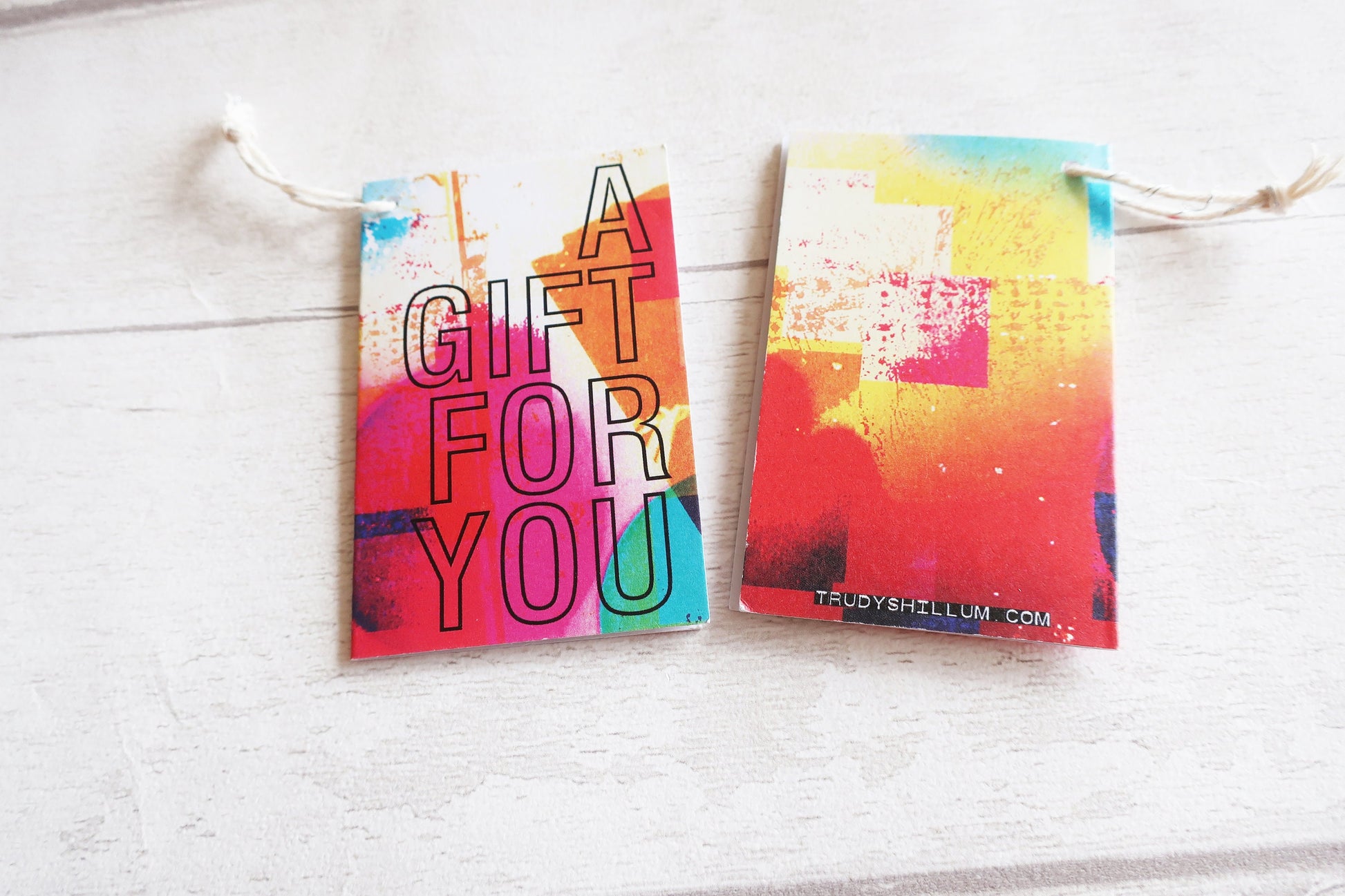 Two colorful gift tags with 'A Gift For You' text on a white wooden surface.