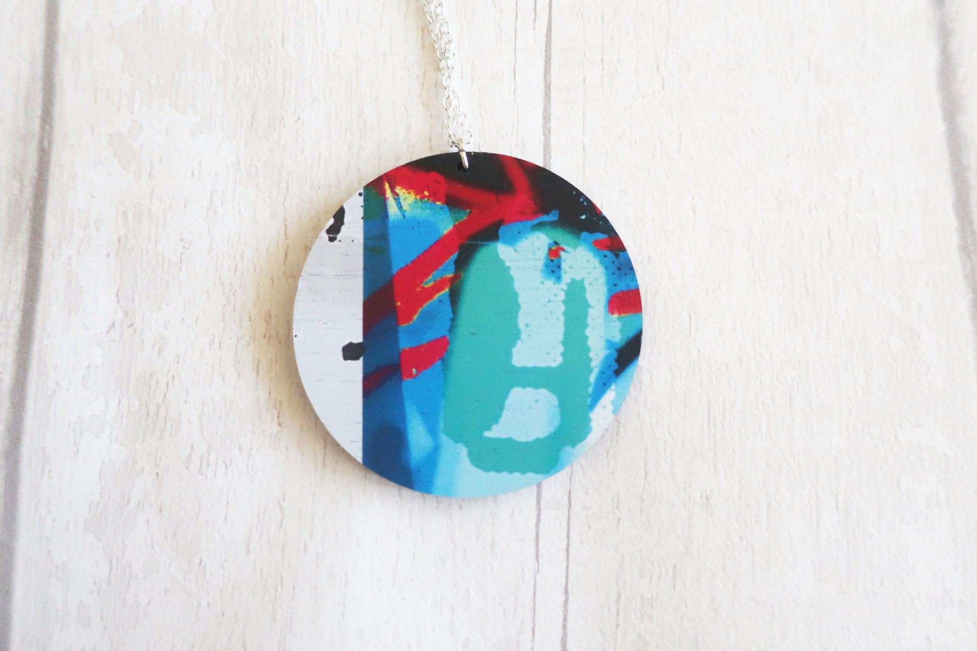 Round decorative necklace with colorful abstract design on a white wooden surface