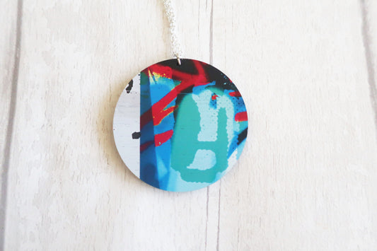 Round decorative necklace with colorful abstract design on a white wooden surface