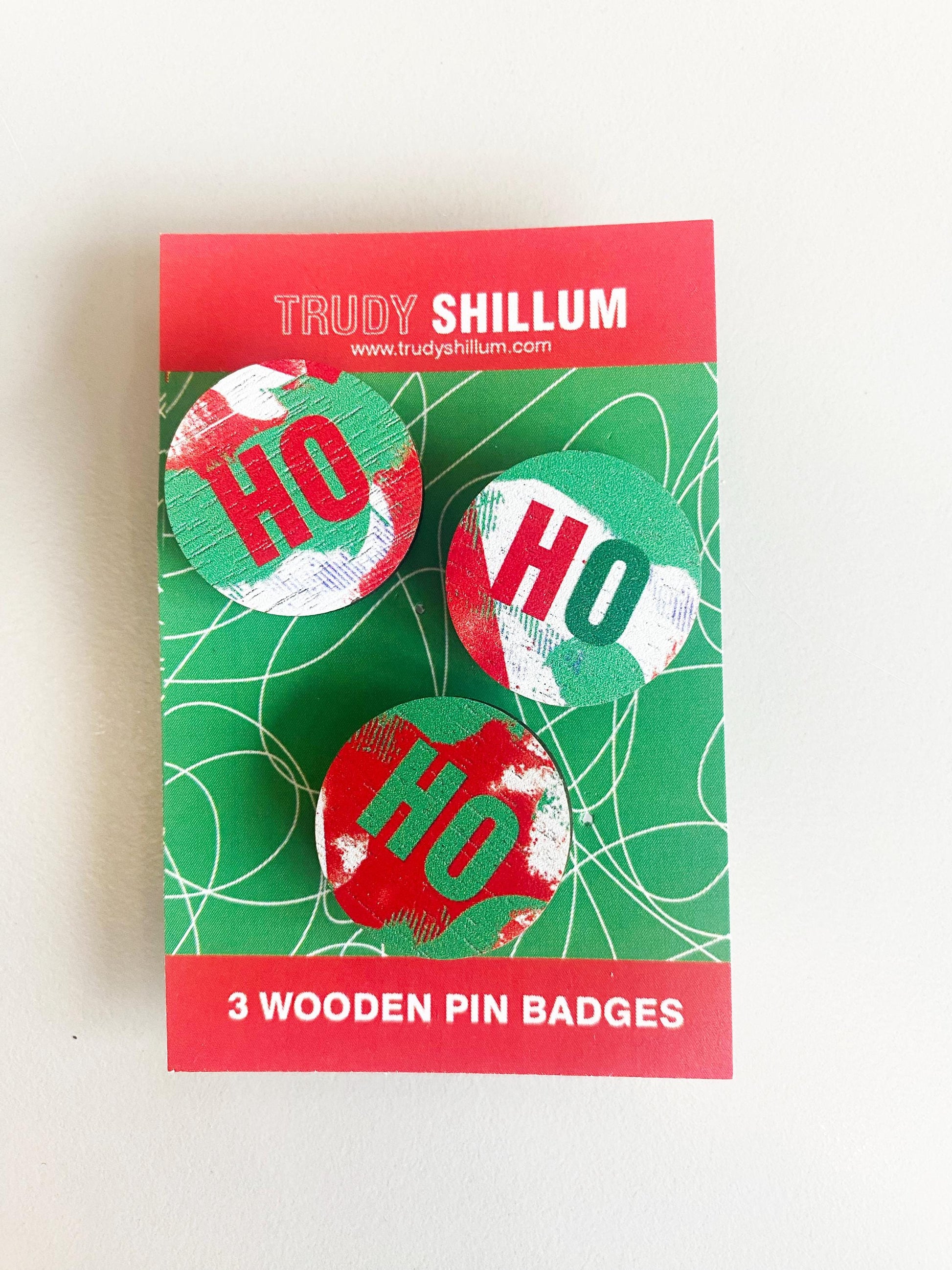 Packaging of Trudy Shillum wooden pin badges with 'HO' design on a white background