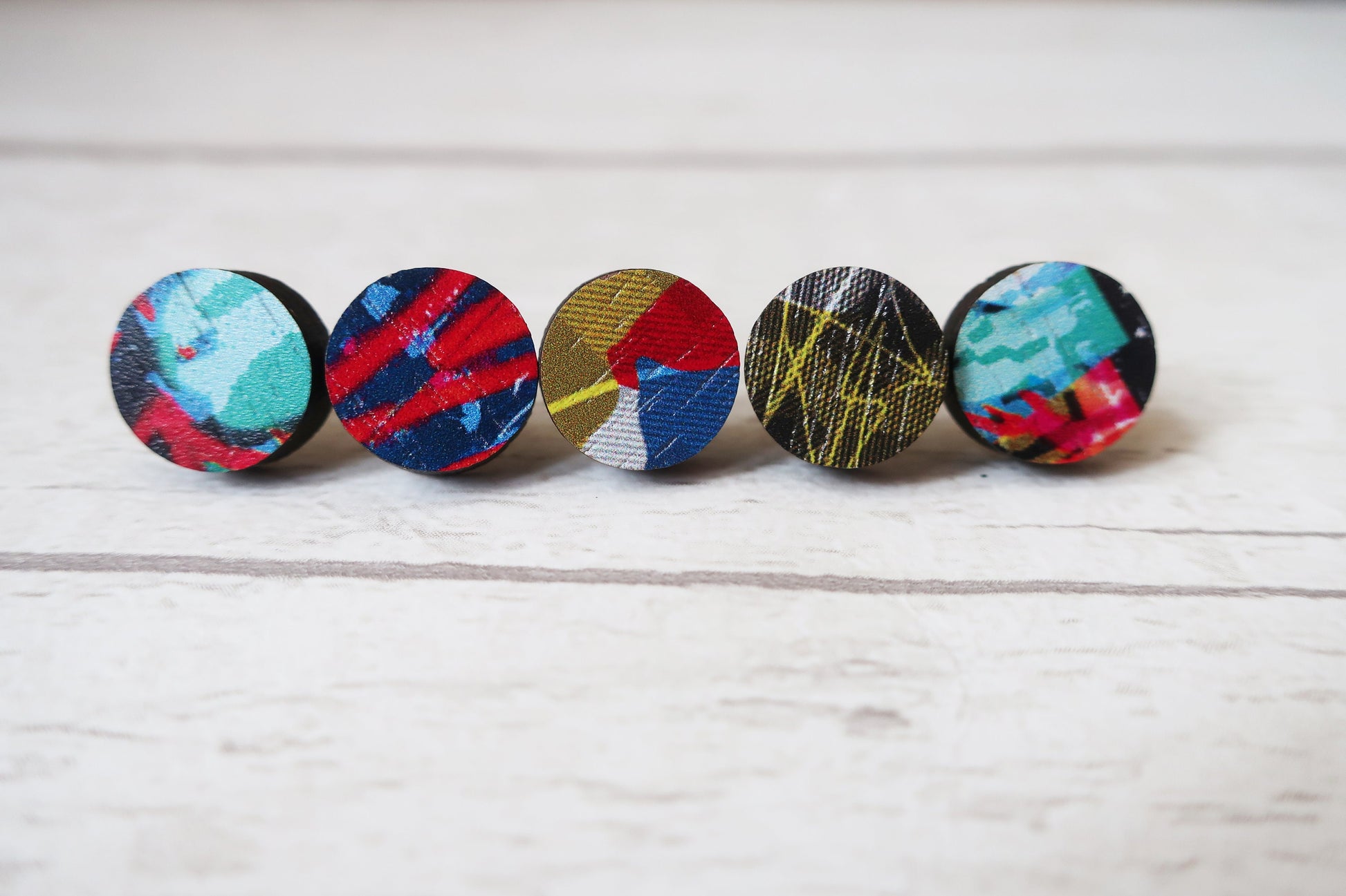 Five colorful round earrings on a light wooden surface