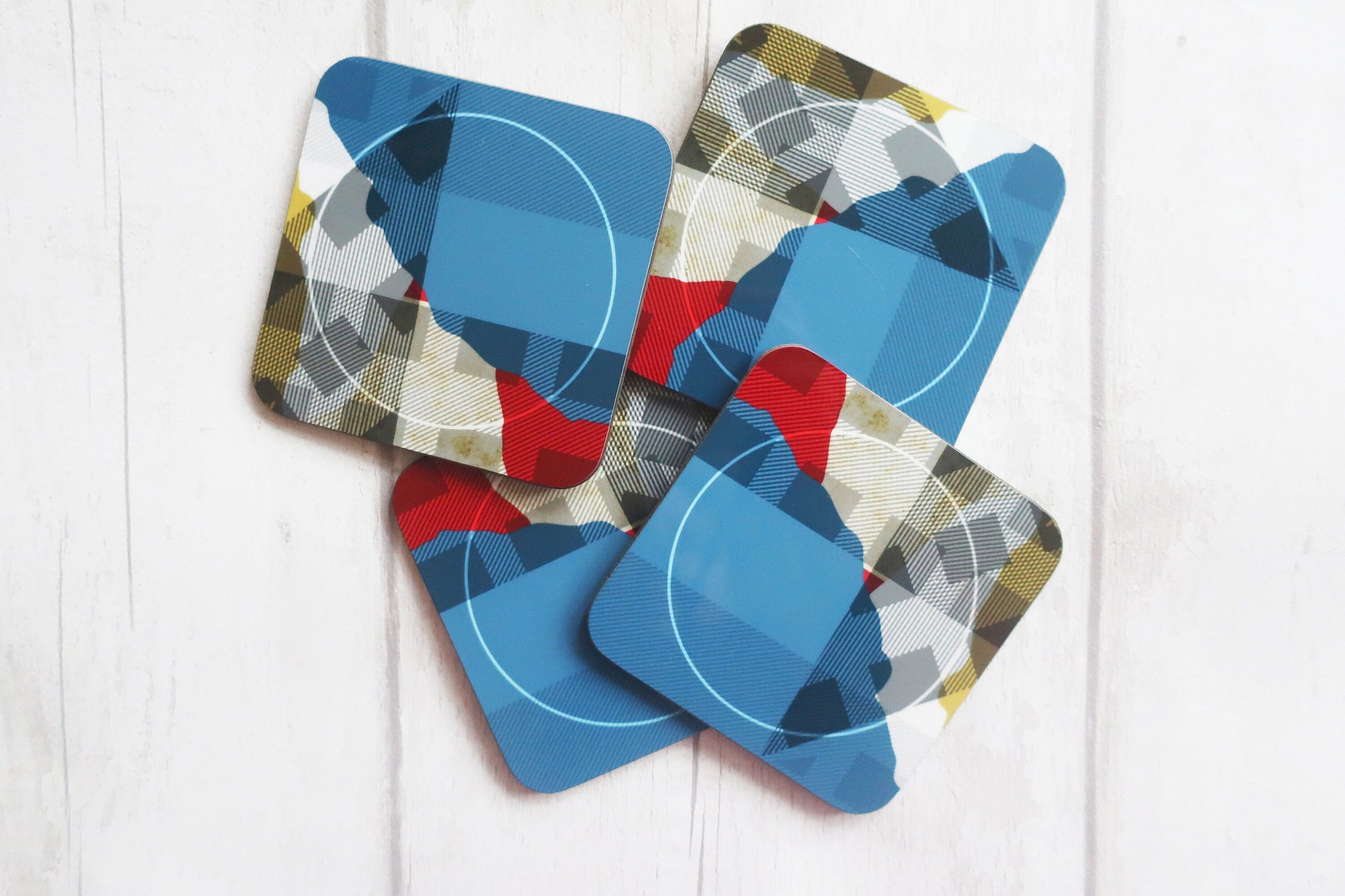 Set of four geometric-patterned coasters on a white wooden surface