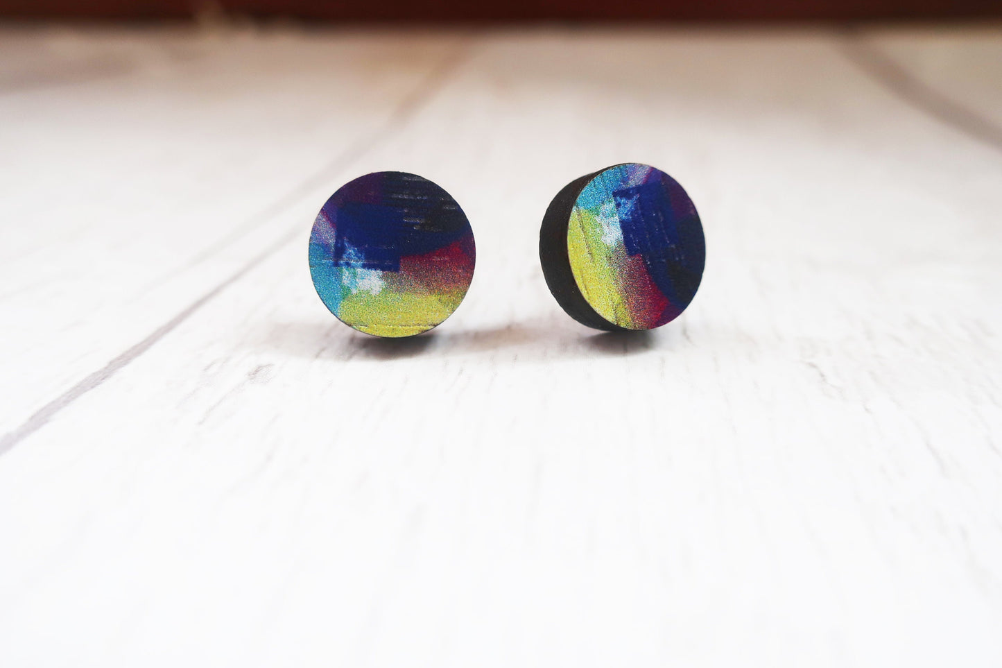 Pair of round rainbow-colored earrings on a light wooden surface.