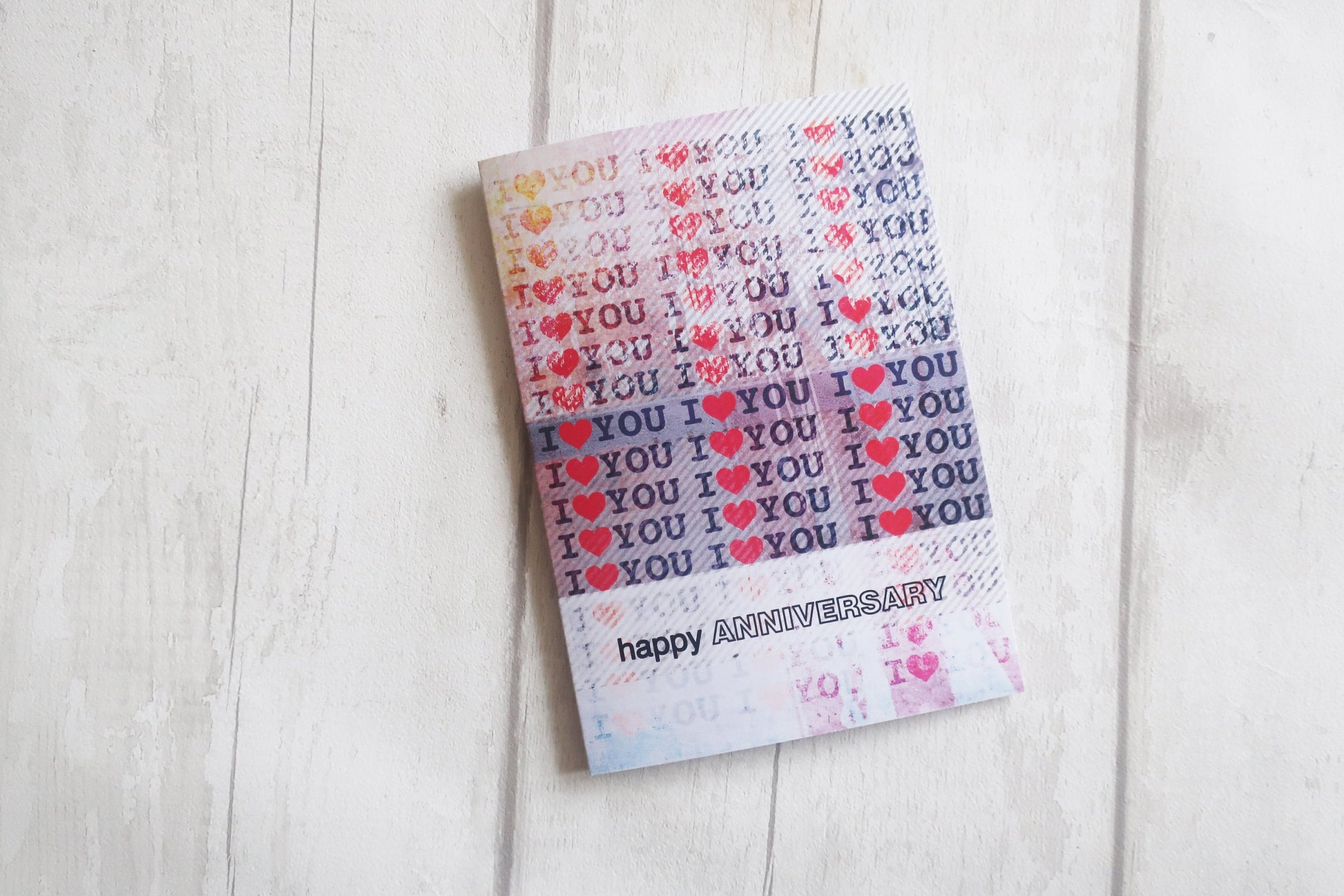 Card with 'YOU' and heart patterns and 'happy anniversary' text on a light wooden surface