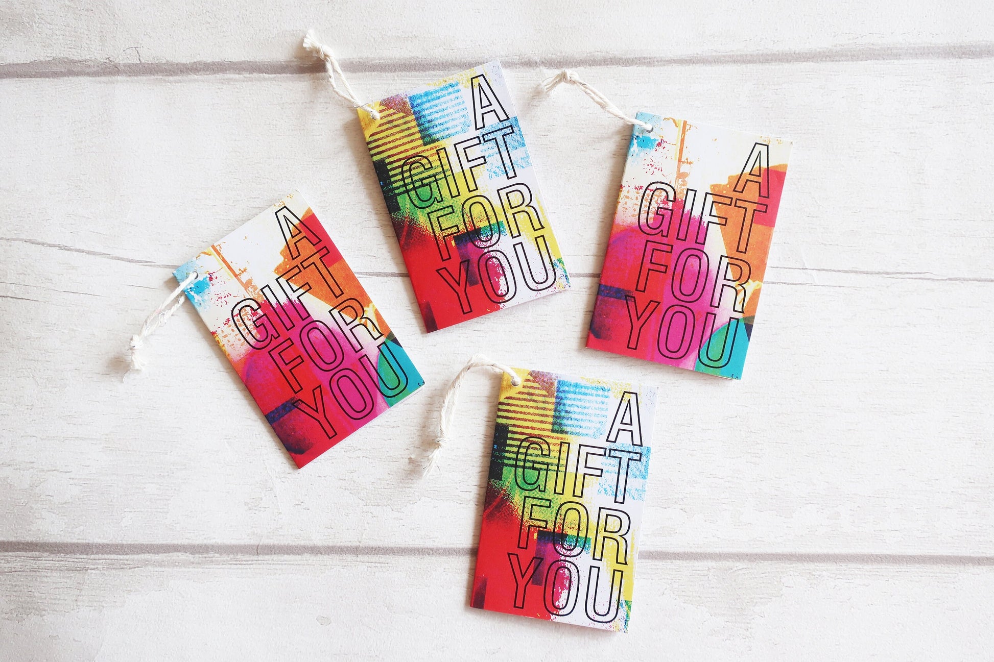 Four colorful 'A Gift For You' tags on a wooden surface