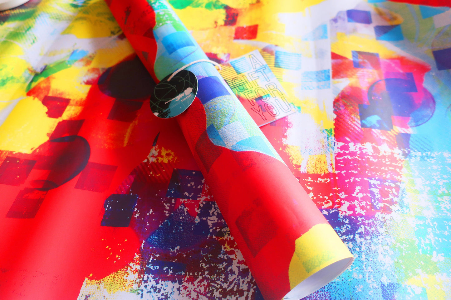 Colorful patterned paper with a roll of red fabric on top