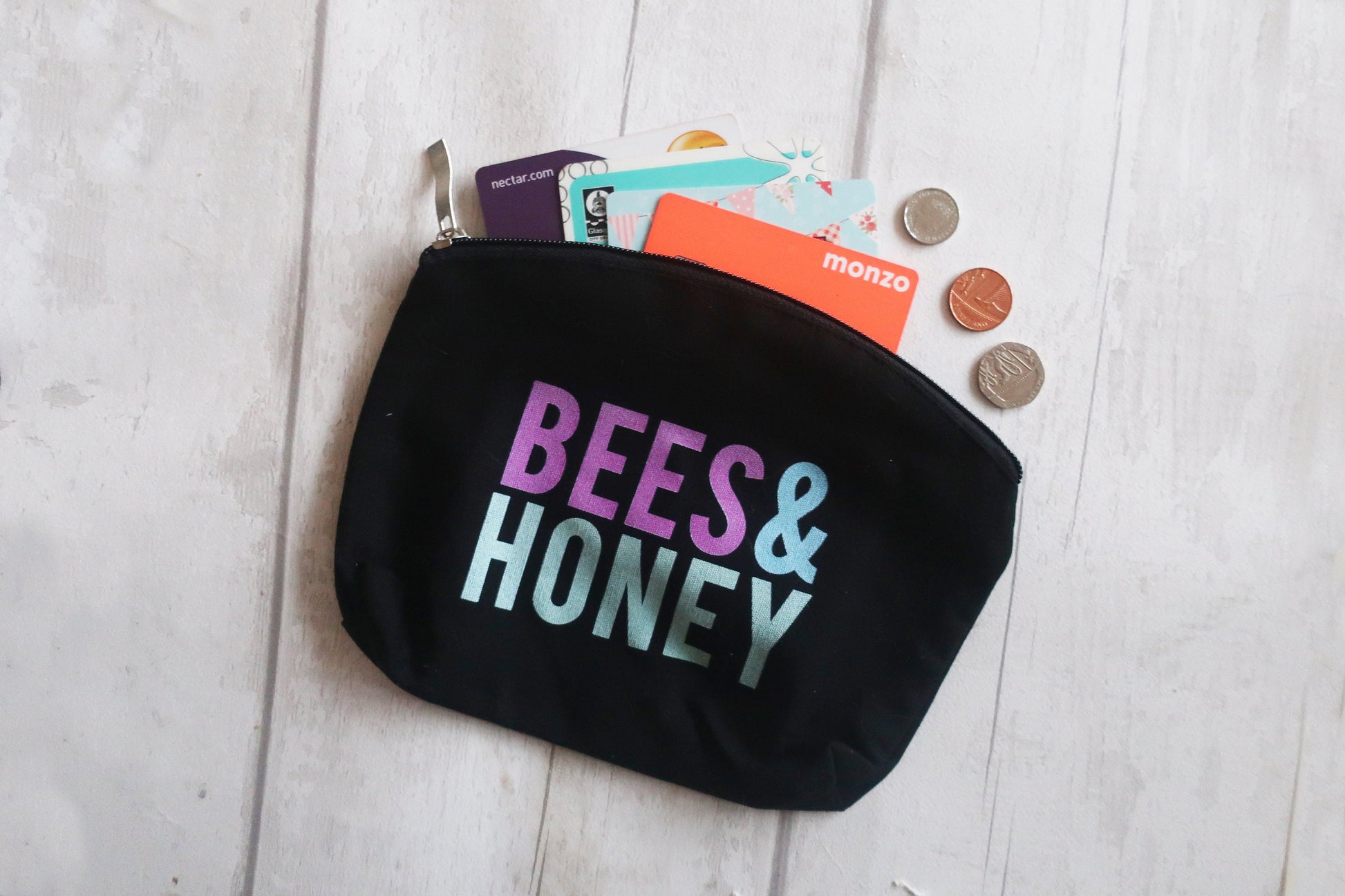 Black pouch with 'BEES & HONEY' text, containing cards and coins on a light wooden surface.