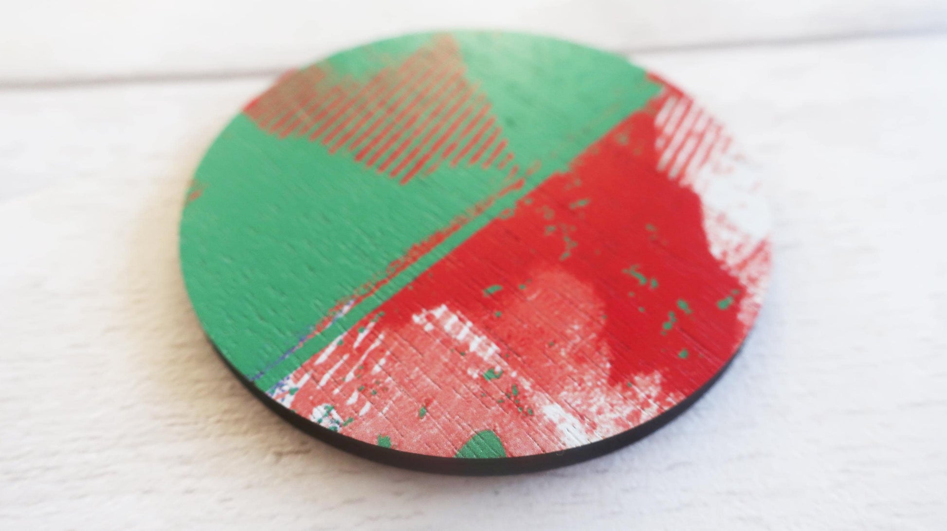 Round brooch with green and red design on a white surface