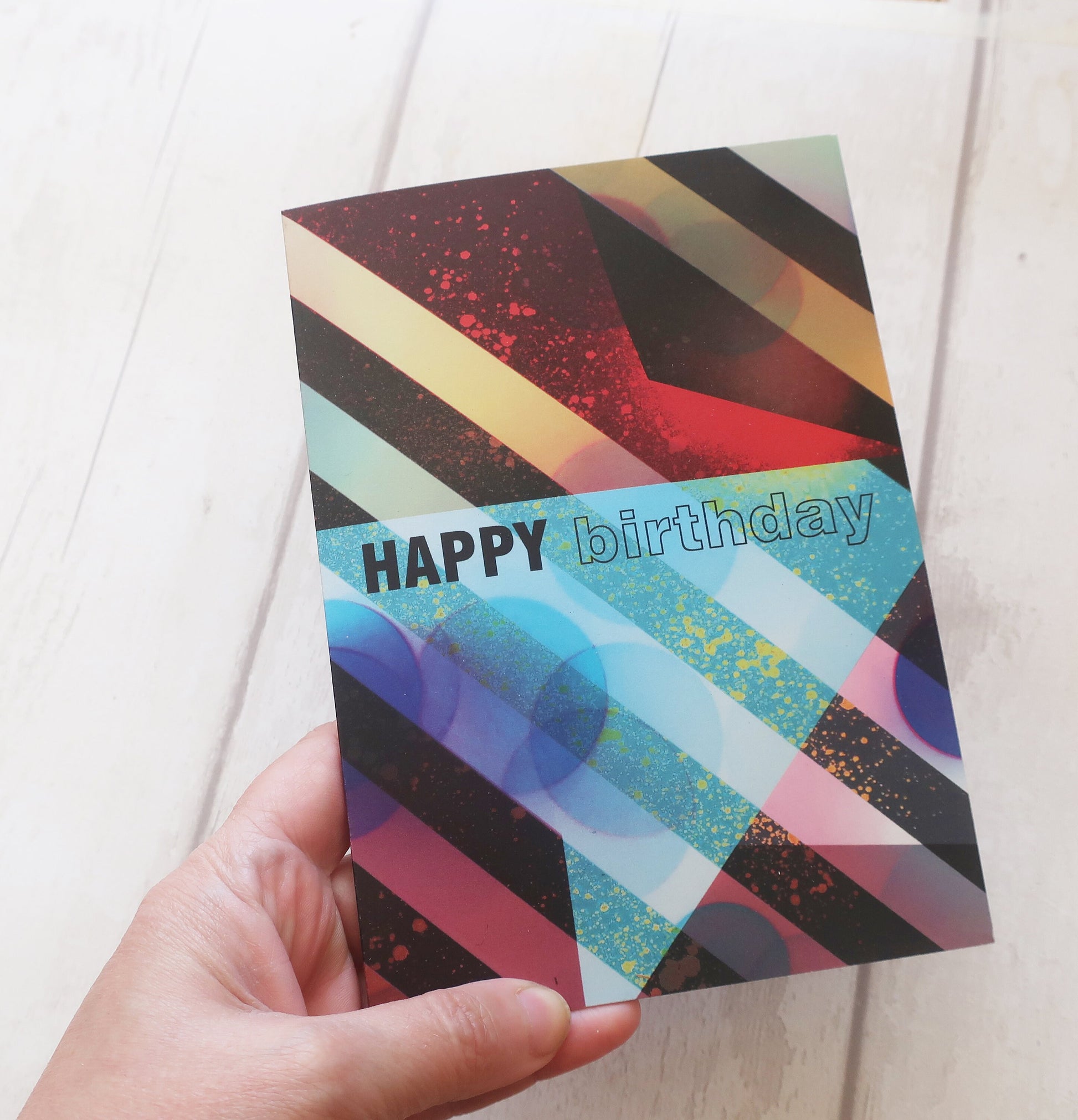 Colorful birthday card with geometric pattern held by a hand on a light background