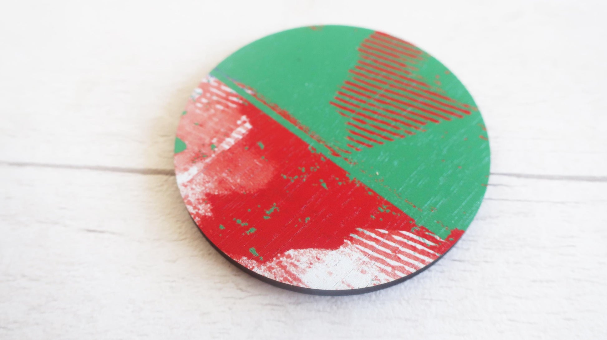 Round brooch with red and green abstract design on a white wooden surface