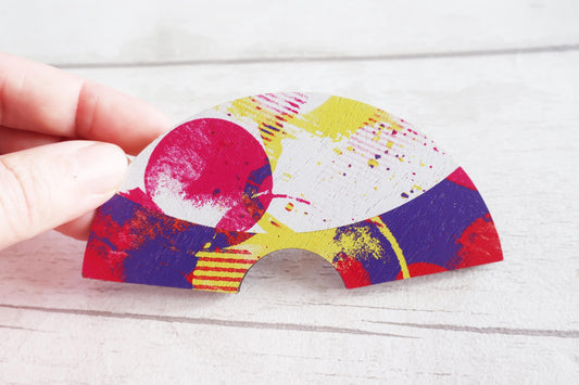 Colorful abstract design on a  fan hairclip held by a hand against a light wooden background