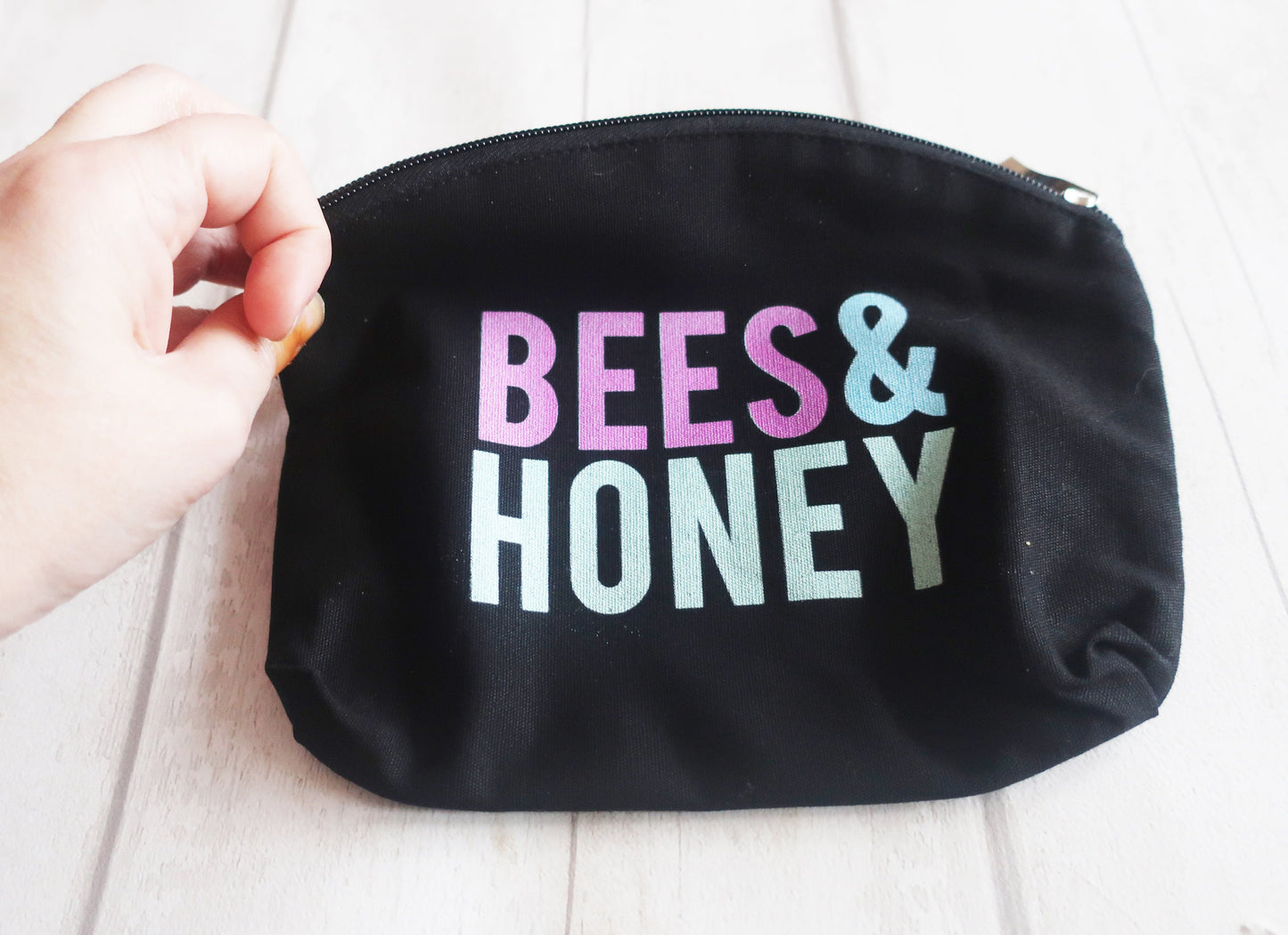 Black pouch with 'BEES & HONEY' text in colorful letters held by a hand.