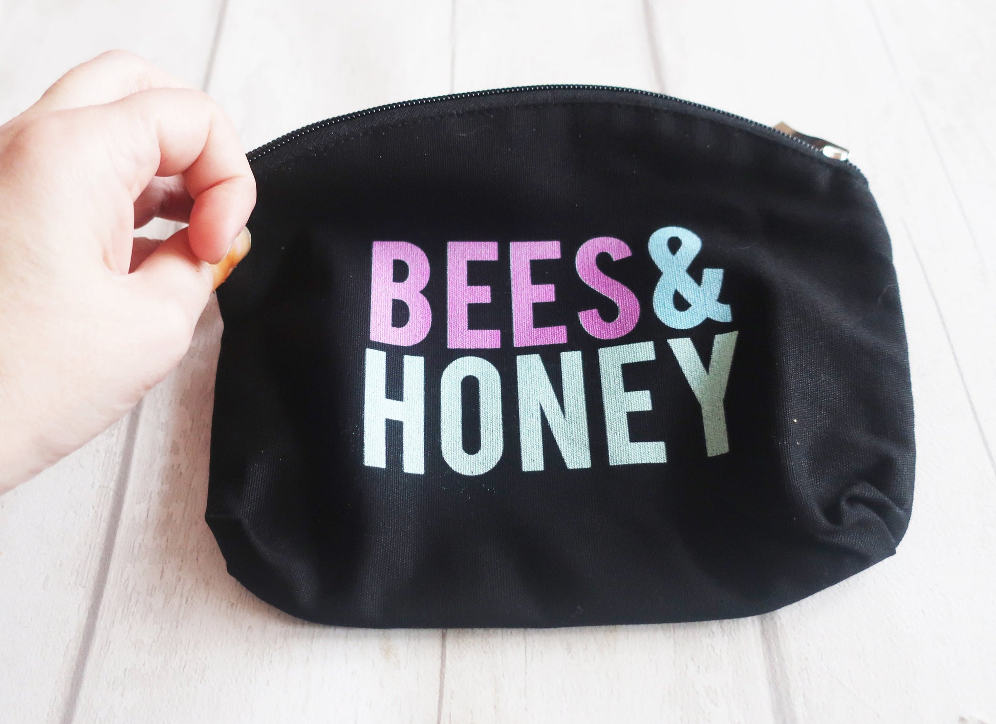 Black pouch with 'BEES & HONEY' text in colorful letters held by a hand.